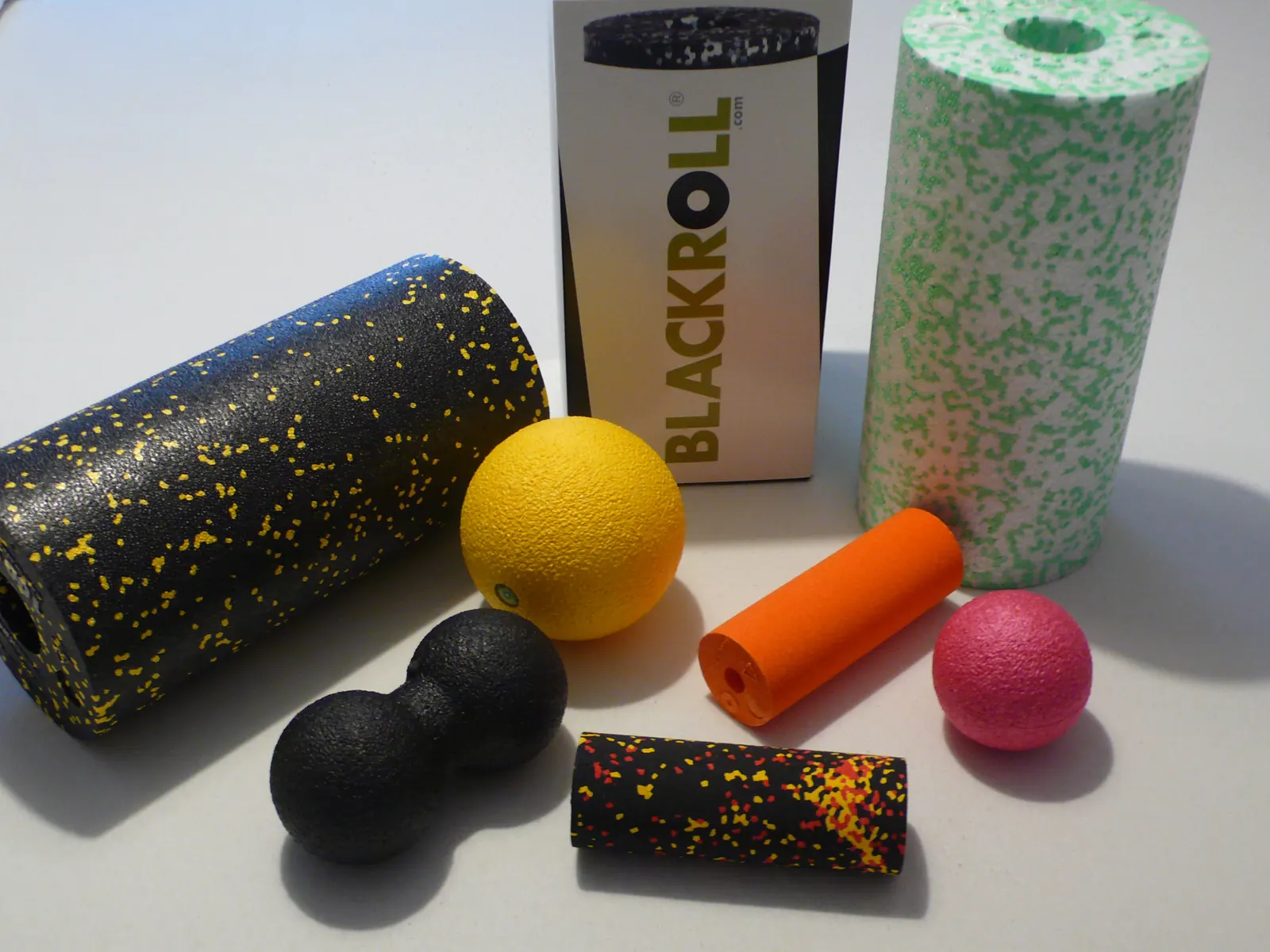 BLACKROLL-Produkte: Faszienrollen in verschiedenen Größen, Duoball, Kugeln und eine Mini-Rolle auf hellem Untergrund