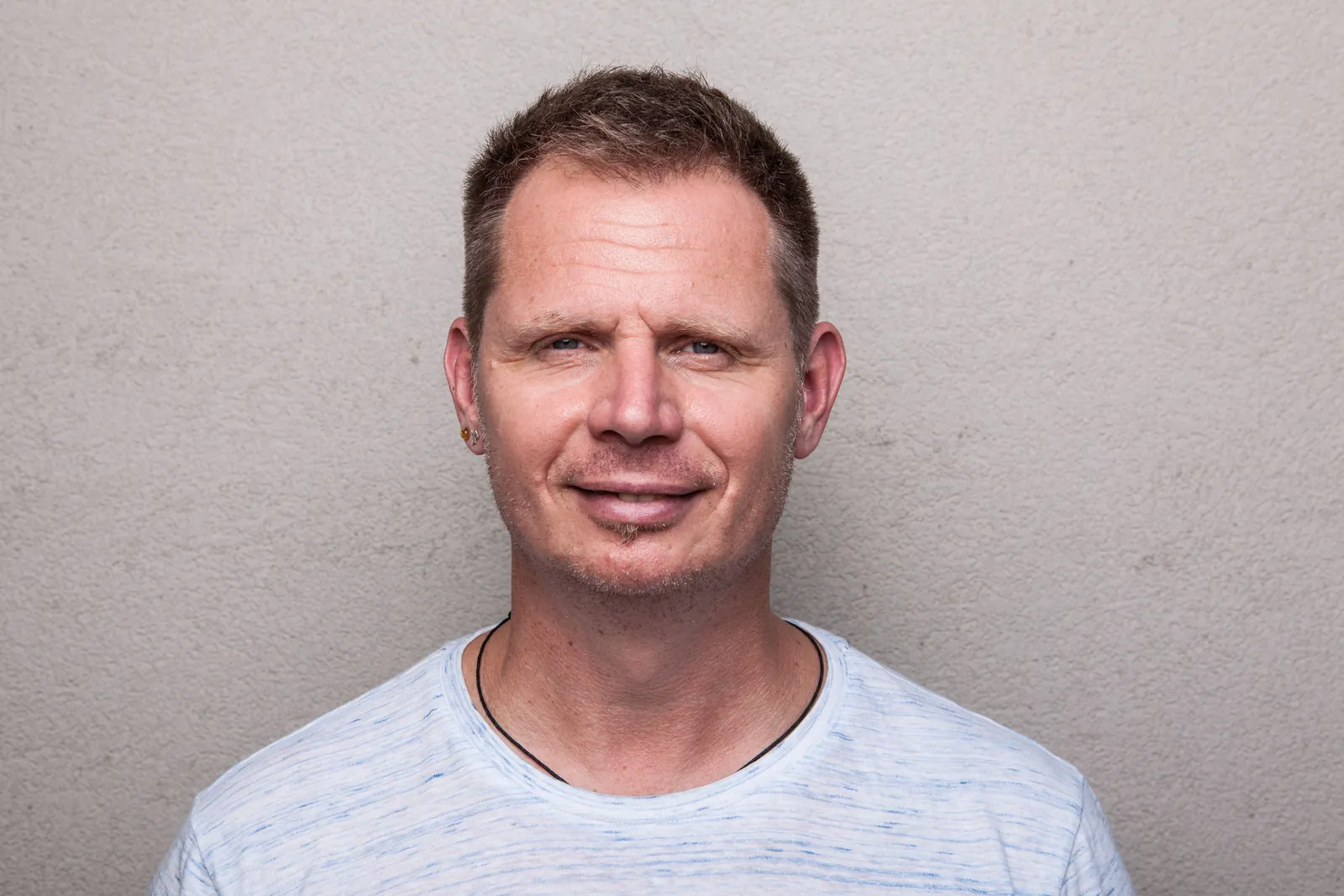 Porträt von Michael Jahn im hellblauen T-Shirt vor einer hellen Wand